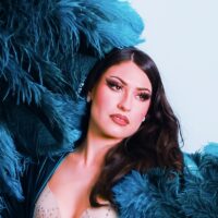 Headshot of a dark-haired individual, wearing a blue feathered robe.