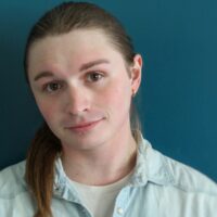 Headshot of an individual, wearing a light-colored collared shirt over a t-shirt, and has ear pierced