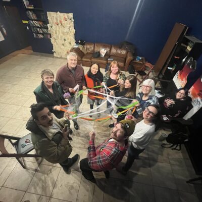 Image of nine people in a circle, holding onto tangled string, looking into the air towards the photographer.